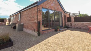 A brick building with large glass sliding doors, gravel ground, and a small garden area with potted plants. - Swallow Cottage (Sandbach)
