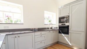 A modern kitchen with white cabinets, a black countertop, and a Bosch oven. - Swallow Cottage (Sandbach)