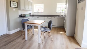 A modern kitchen with white cabinets, a wooden table, two chairs, and a refrigerator. - Swallow Cottage (Sandbach)