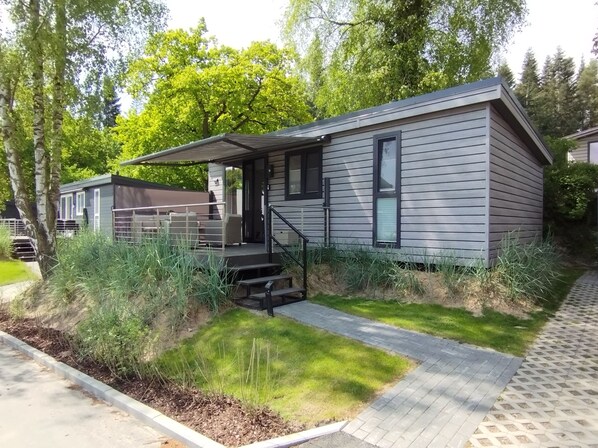 Ein modernes eingeschossiges Haus mit überdachter Veranda, einer kleinen Terrasse und einem Vorgarten mit einem Weg zum Eingang.