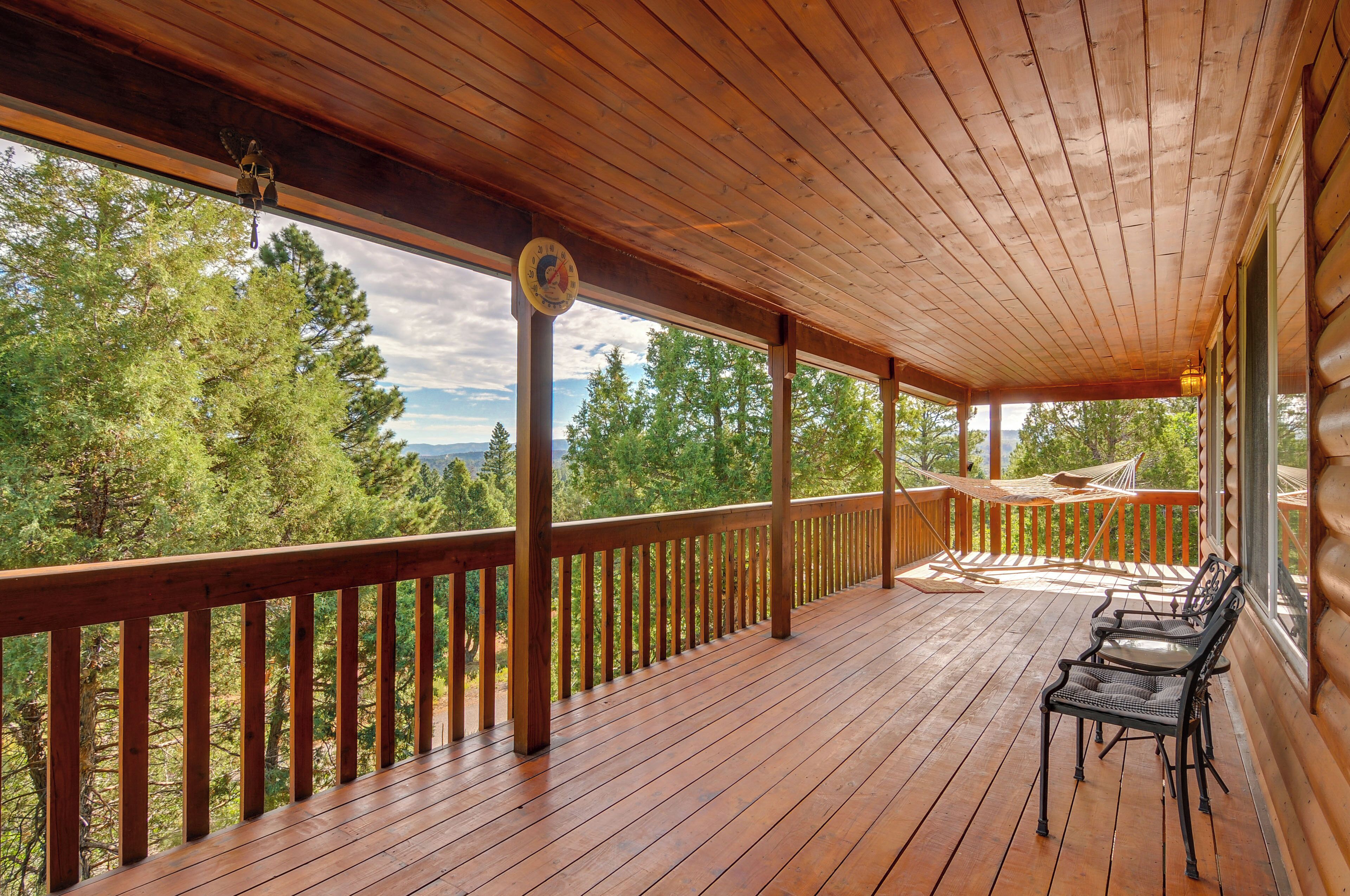 Une terrasse en bois avec un hamac et des chaises, donnant sur une zone boisée.
