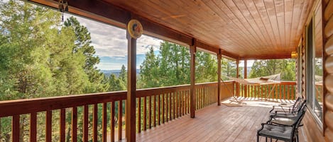 A wooden deck with a hammock and chairs, overlooking a forested area.