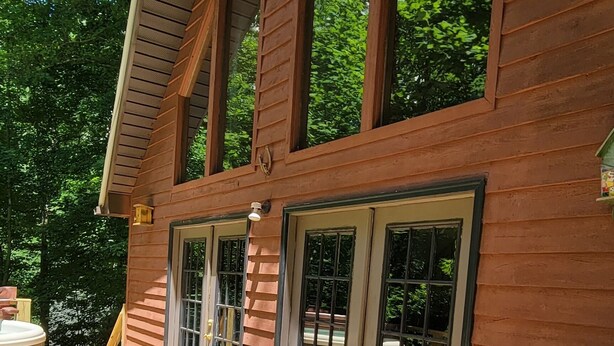 A wooden deck with a hot tub and two chairs, a covered patio area, and large windows. - Cabin near Fontana and NOC (Bryson City)