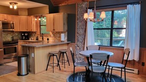 A modern kitchen with wooden cabinets, stainless steel appliances, and a central island with bar stools. - Cabin near Fontana and NOC (Bryson City)