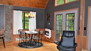 A cozy room with a wooden ceiling, a dining table with chairs, a black leather chair, and large windows with curtains. - Cabin near Fontana and NOC (Bryson City)
