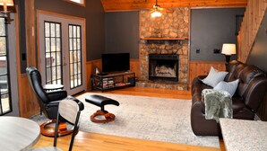 A cozy living room with a stone fireplace, leather sofas, and a television. - Cabin near Fontana and NOC (Bryson City)
