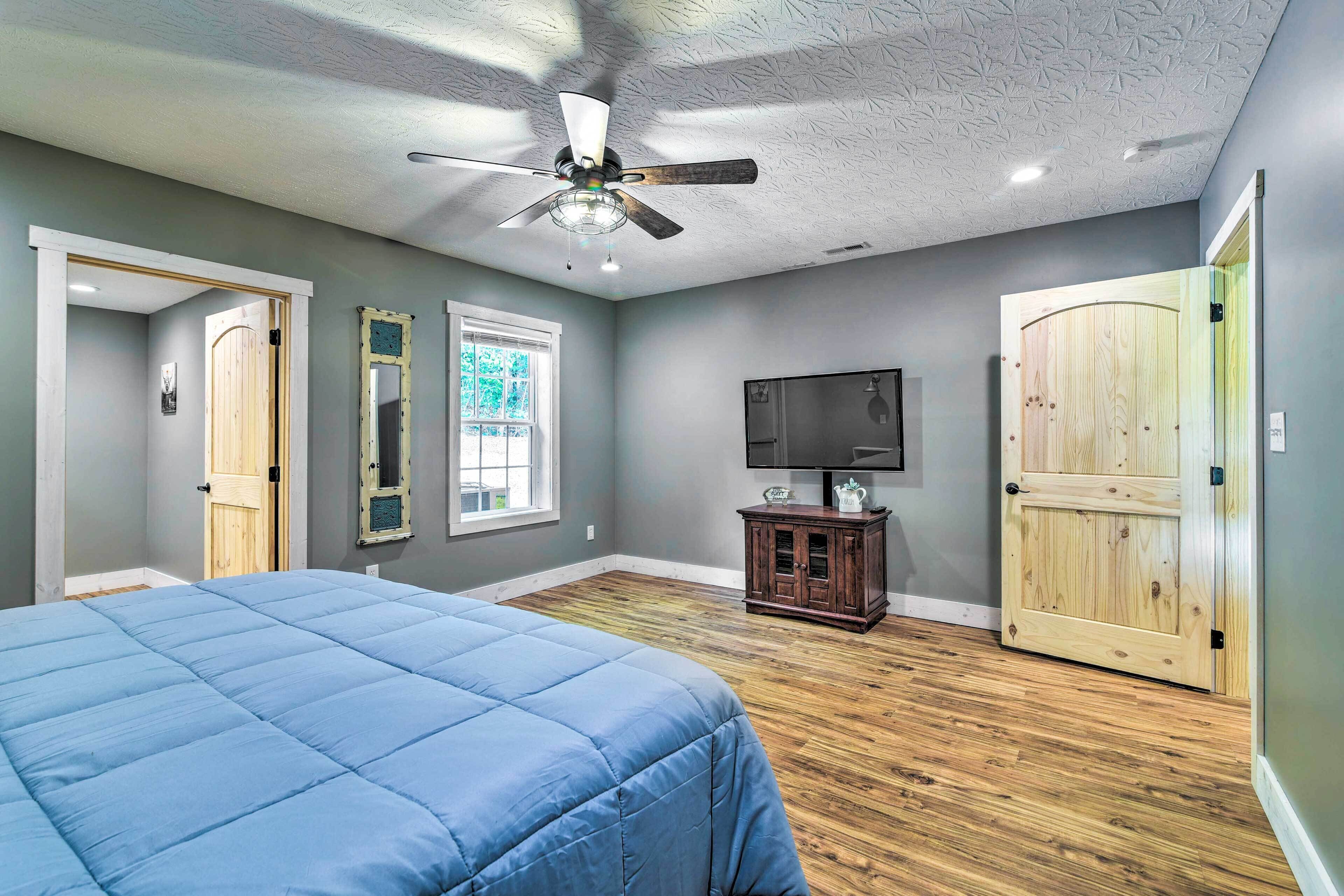 A bedroom with a bed, a ceiling fan, a television, and wooden flooring.