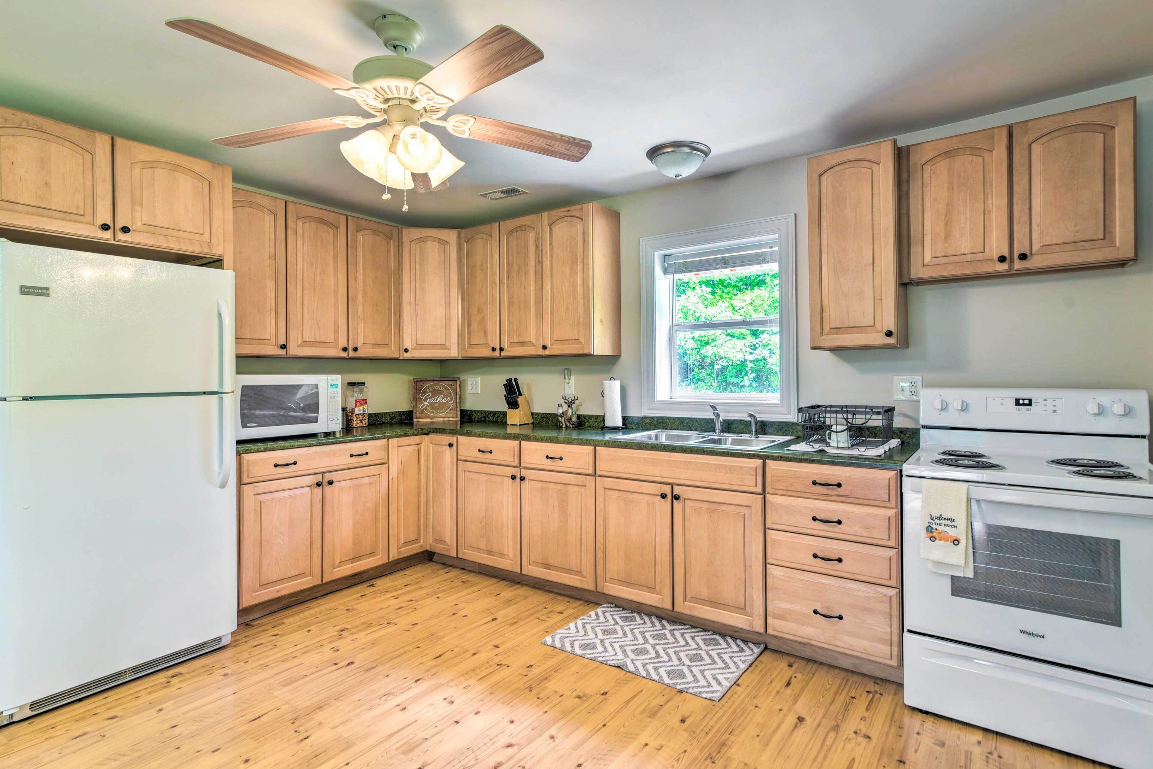 A kitchen with wooden cabinets, a refrigerator, microwave, stove, and a ceiling fan.