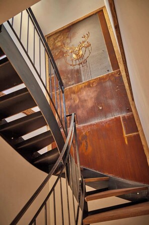 A spiral staircase with metal railings and wooden steps leading to a door with a decorative emblem. - Spirit of Deer – Private Sauna & Hot Tub (Garmisch-Partenkirchen)