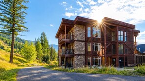 A multi-story lodge with a stone facade, multiple balconies, and a view of the surrounding forest.