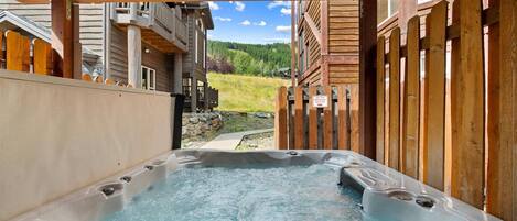 A hot tub area with a wooden deck and a view of a mountain landscape.