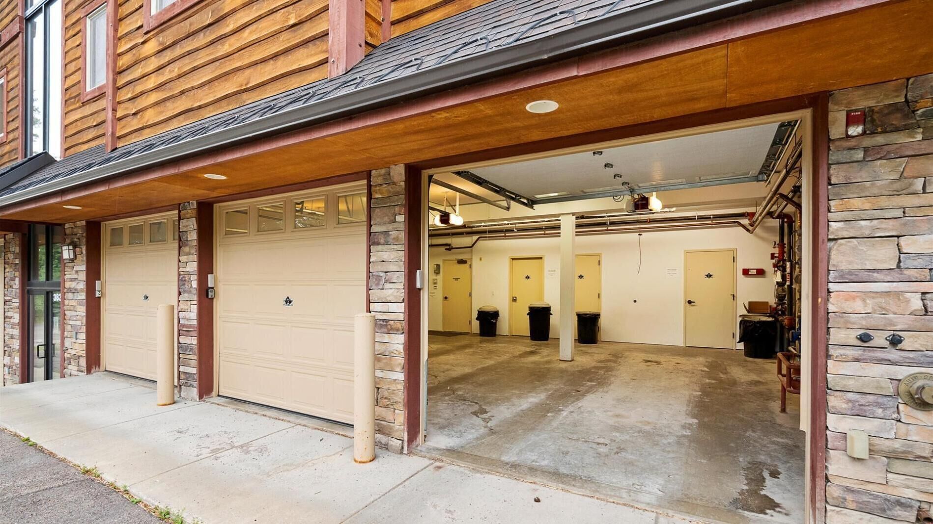 A garage with two large doors, a concrete floor, and a stone wall on one side.