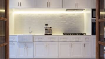 A modern kitchen with white cabinets, a tiled backsplash, a coffee maker, and a stove.