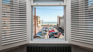 A view from a window with blinds, overlooking a parking lot and buildings, with a clear sky and a distant view of the sea. - Serenity by the Sea - Broadstairs (Kent)