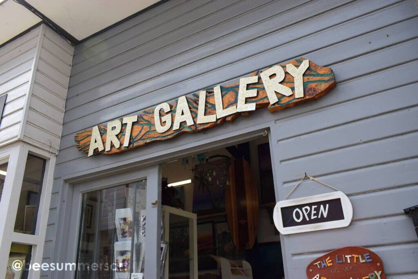 Een kunstgalerie met een houten naambordje en een 'OPEN' bord.