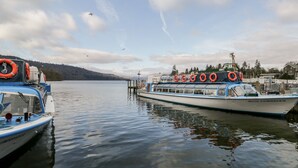 Un ferry atracado en un muelle, con un lago tranquilo y montañas al fondo.