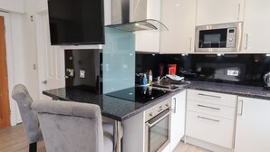 Una cocina moderna con televisor de pantalla plana, electrodomésticos de acero inoxidable y una silla tapizada en gris.