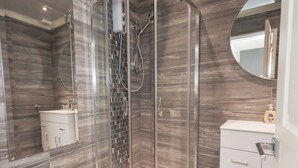 Un baño moderno con ducha envuelta en vidrio, tocador blanco y un espejo grande.