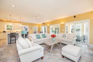 A spacious living area with a large white sofa, a coffee table, and a kitchen area with a bar.