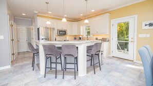 A kitchen with a central island, bar stools, pendant lighting, and a view through a glass door. - MAIN LAKE VIEWS - Fire Pit - Kayaks, SUPs - Pool Table - Bikes (Littleton)