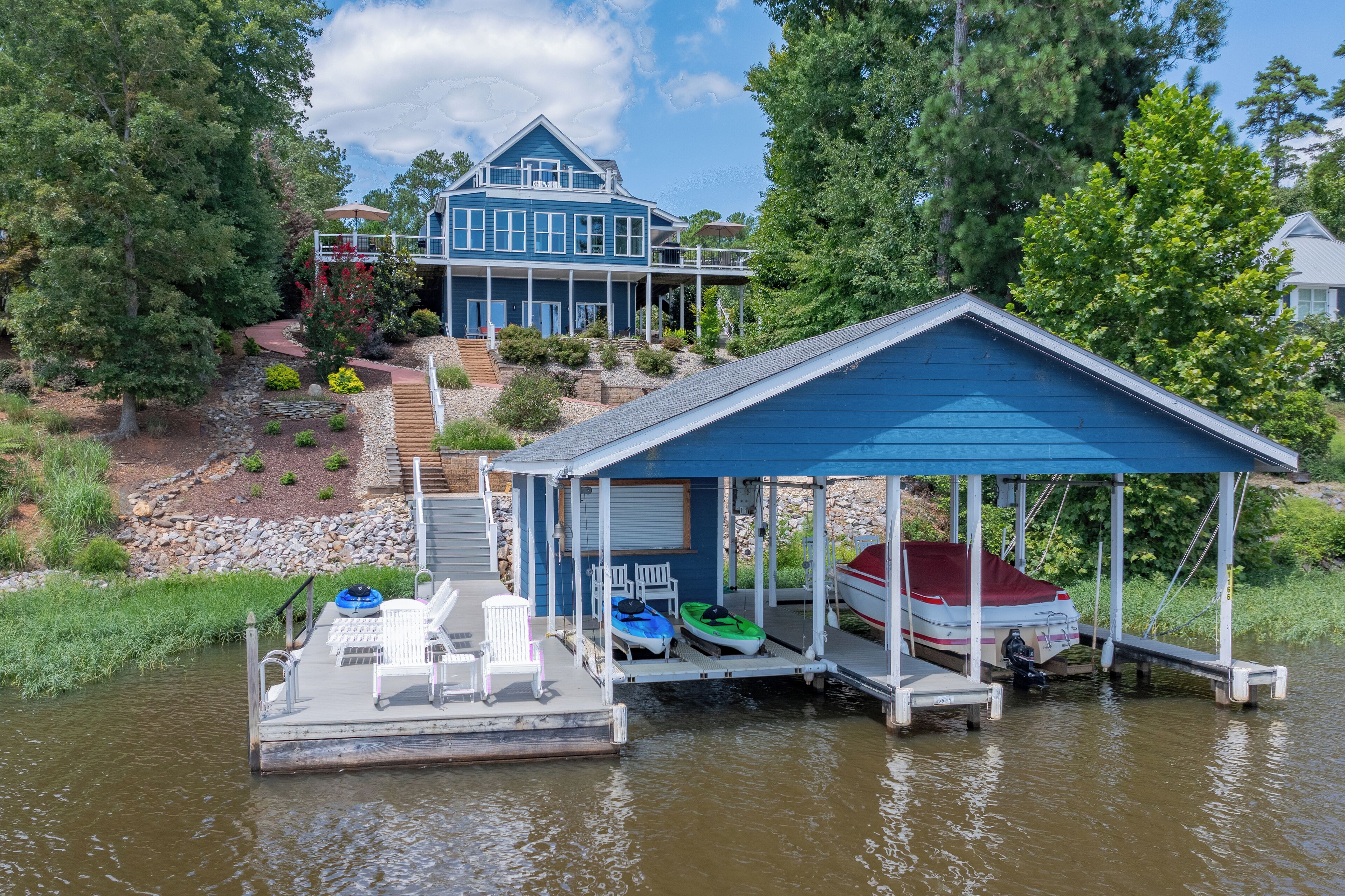 A dock with a covered seating area, a boat, and a house in the background.