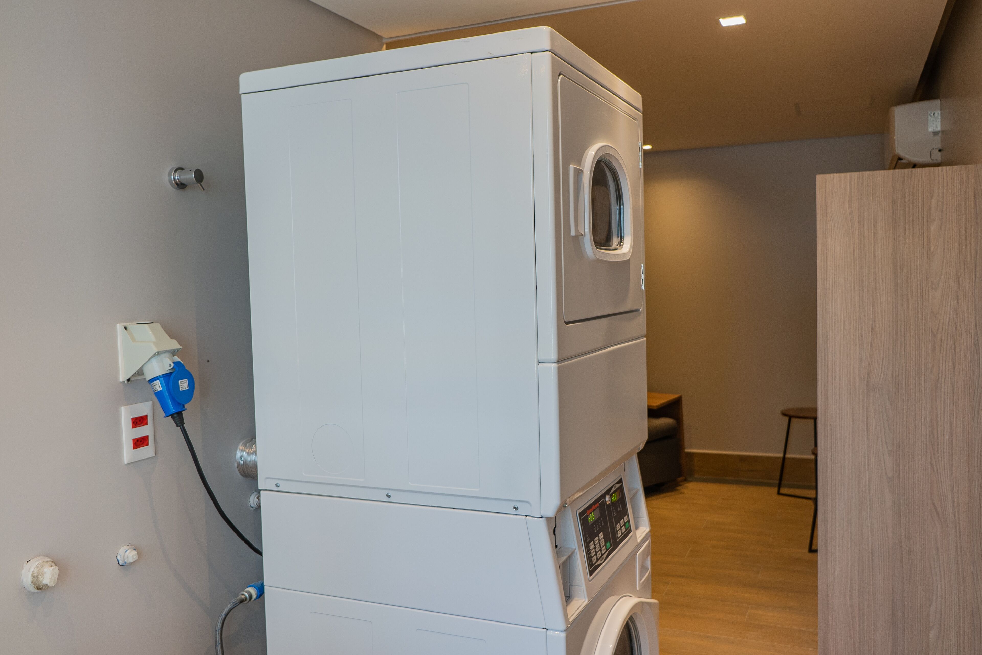 A stacked washer and dryer unit in a room with a wooden floor and a small table.
