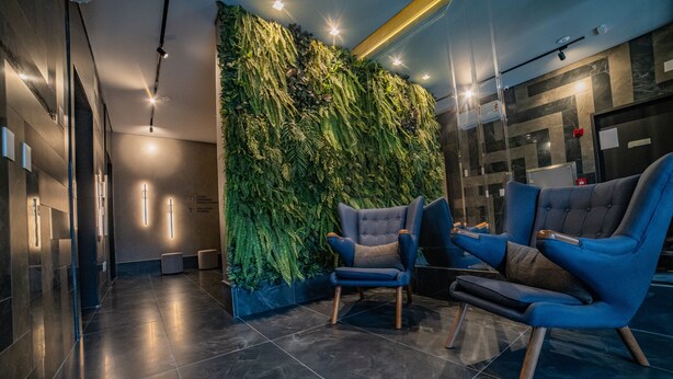 A modern lobby with a vertical garden wall, two blue armchairs, and a dark tiled floor.