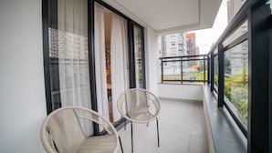 A balcony with two wicker chairs, a sliding glass door, and a view of a cityscape.