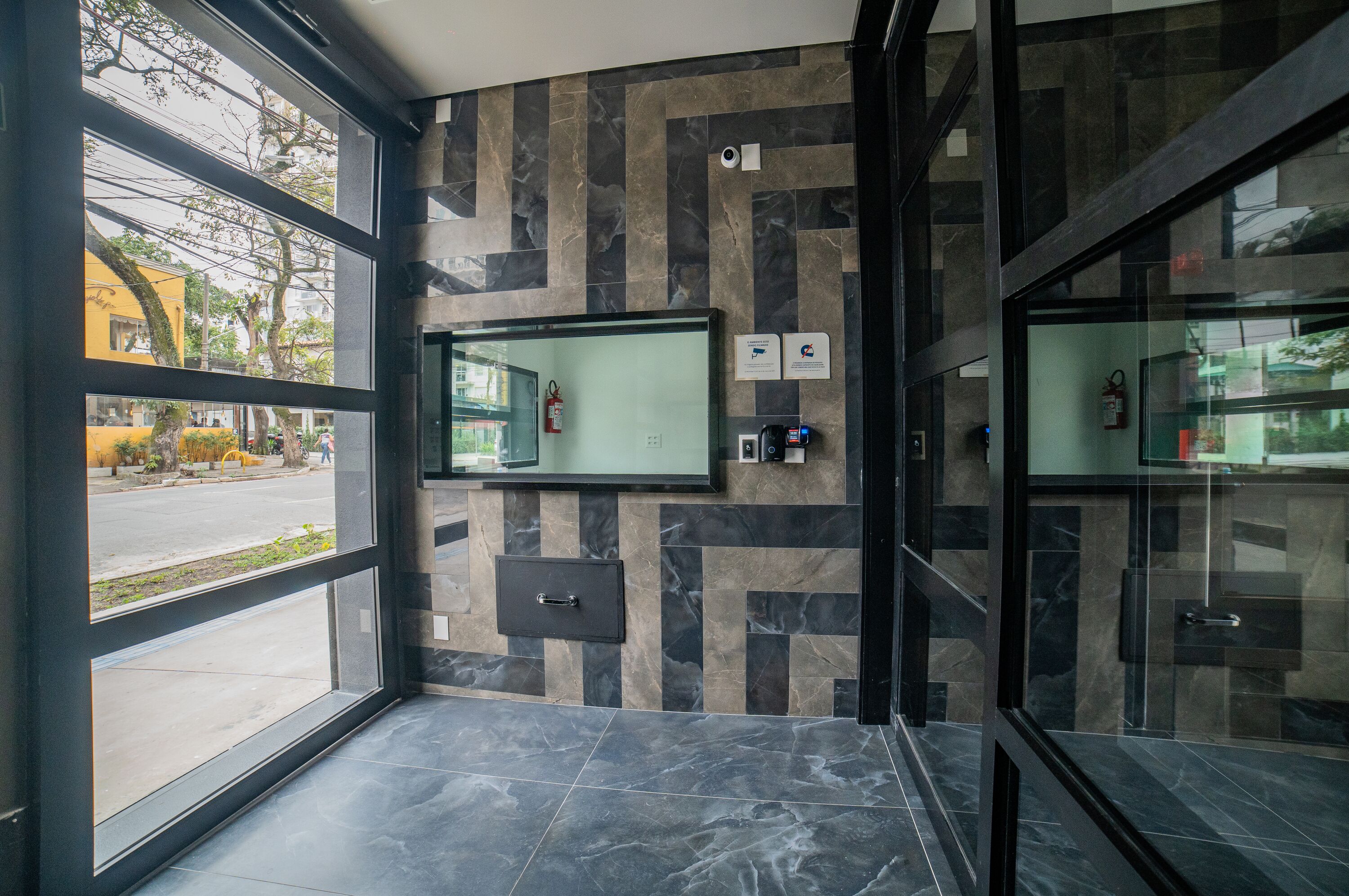 A modern lobby with a glass door, a fire extinguisher, a security camera, and a digital information kiosk.
