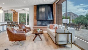 A modern living room with a fireplace, leather sofas, a dining area, and large windows offering a mountain view. - Resort Style Retreat, Red Rock Views Inside & Out+Salt Water Pool+Hot Tub (Sedona)