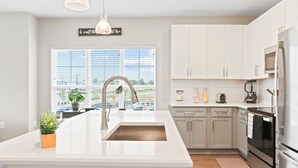 A modern kitchen with white cabinetry, a stainless steel sink, and a large window providing natural light.