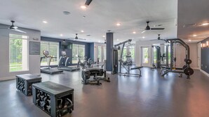 A spacious gym with various exercise equipment, large windows, and ceiling fans.