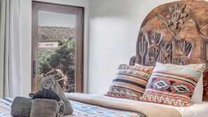 Un lit avec une couvre-lit à motifs, deux oreillers aux motifs géométriques, une sculpture de cactus et une tête de lit en bois ornée d’un motif solaire.