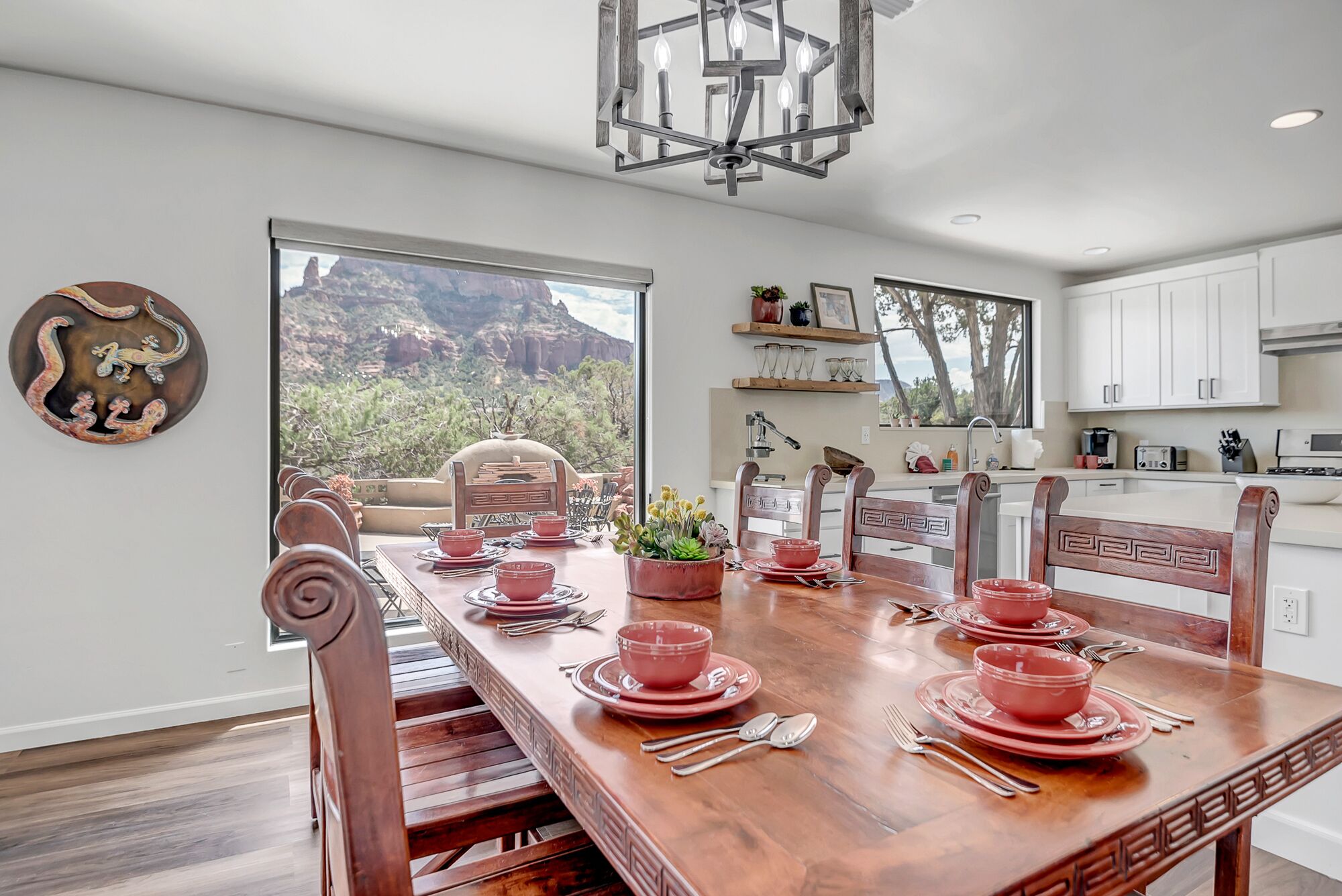 Un coin repas avec une table en bois dressée pour quatre personnes, entourée de chaises. Une grande fenêtre offre une vue sur un paysage montagneux.