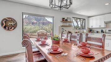 Un coin repas avec une table en bois dressée pour quatre personnes, entourée de chaises. Une grande fenêtre offre une vue sur un paysage montagneux.