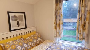 A bedroom with a bed, a bedside table, a framed picture on the wall, and a window with curtains. - Orpington RSG House (Orpington)
