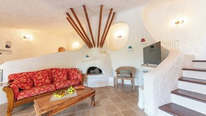 A cozy living room with a red sofa, wooden coffee table, and a fireplace. There is a staircase with a white wall and a flat-screen TV mounted above it. - Villa Isa 6, Emma Villas (Altura)