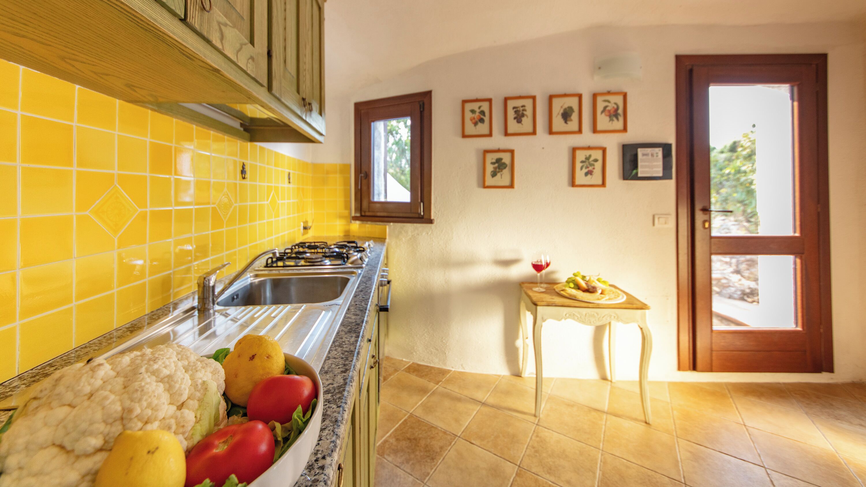 A kitchen with yellow tiles, a sink, a stove, and a dining table with a plate of food.