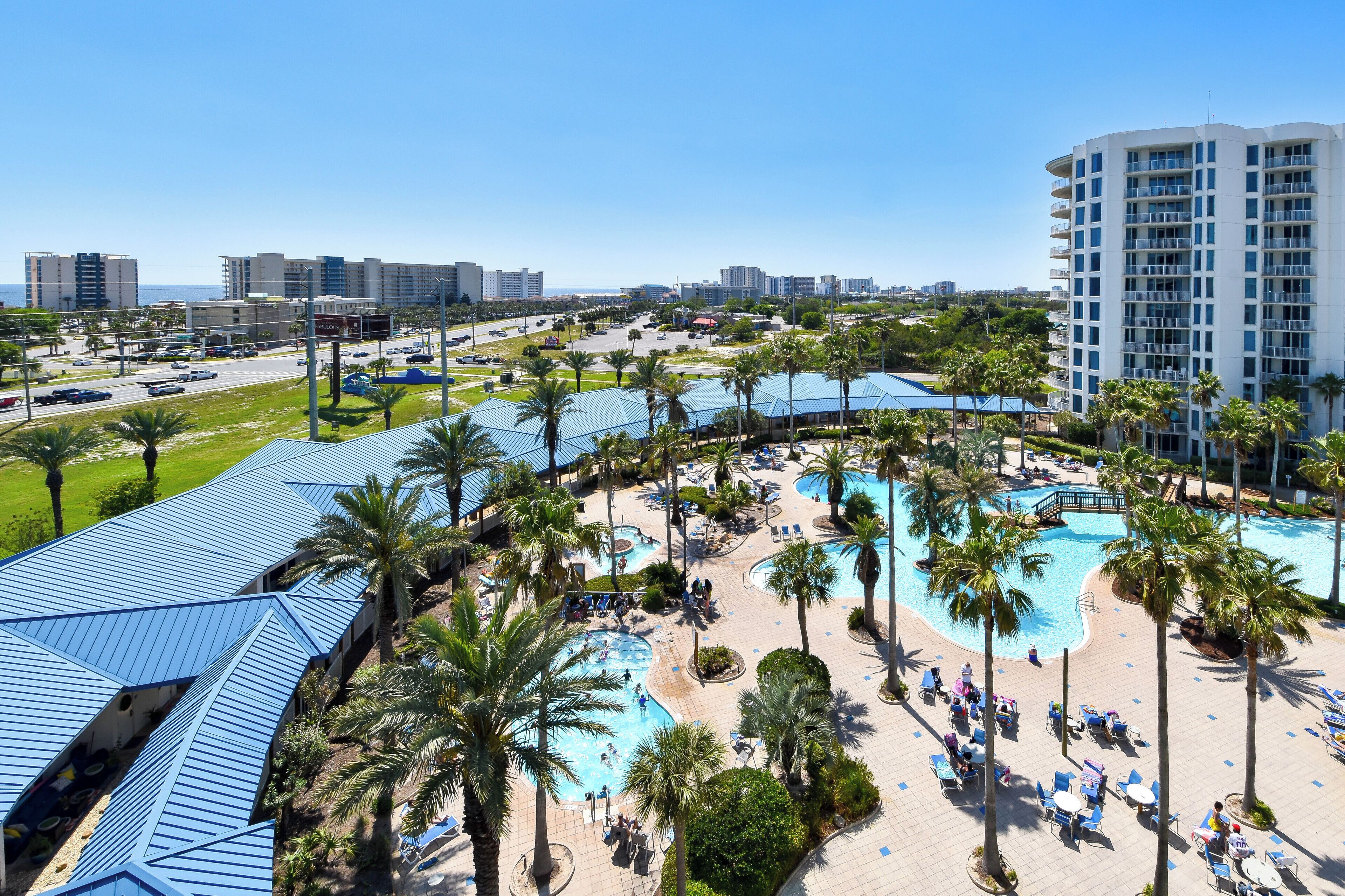 A resort with multiple swimming pools, palm trees, and a large parking area.