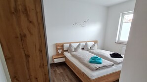 Un dormitorio con estructura de cama de madera, ropa de cama blanca y una mesita de noche.