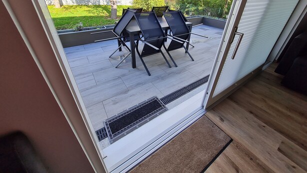 Un patio moderno con una mesa y sillas, vistas al jardín y una puerta corrediza de vidrio.