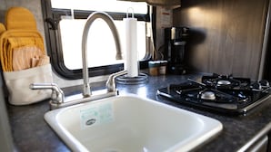 A kitchen with a white sink, stainless steel faucet, and a gas stove. - Charming Winnie Drop Trailer with Cozy Private Patio Escape (Farmington)
