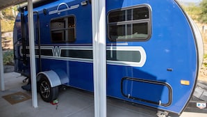 A blue recreational vehicle parked under a covered area with a white roof. - Charming Winnie Drop Trailer with Cozy Private Patio Escape (Farmington)