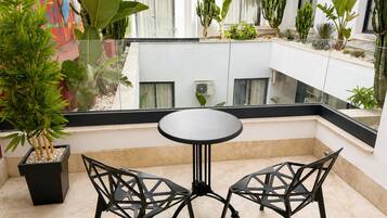 A balcony with a table and chairs, surrounded by various plants and cacti.