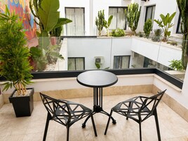 Un balcón con mesa y sillas, rodeado de plantas y cactus.