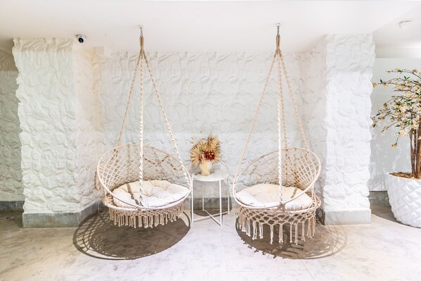 Una habitación con dos sillones colgantes, una mesita con un florero y una planta en maceta.
