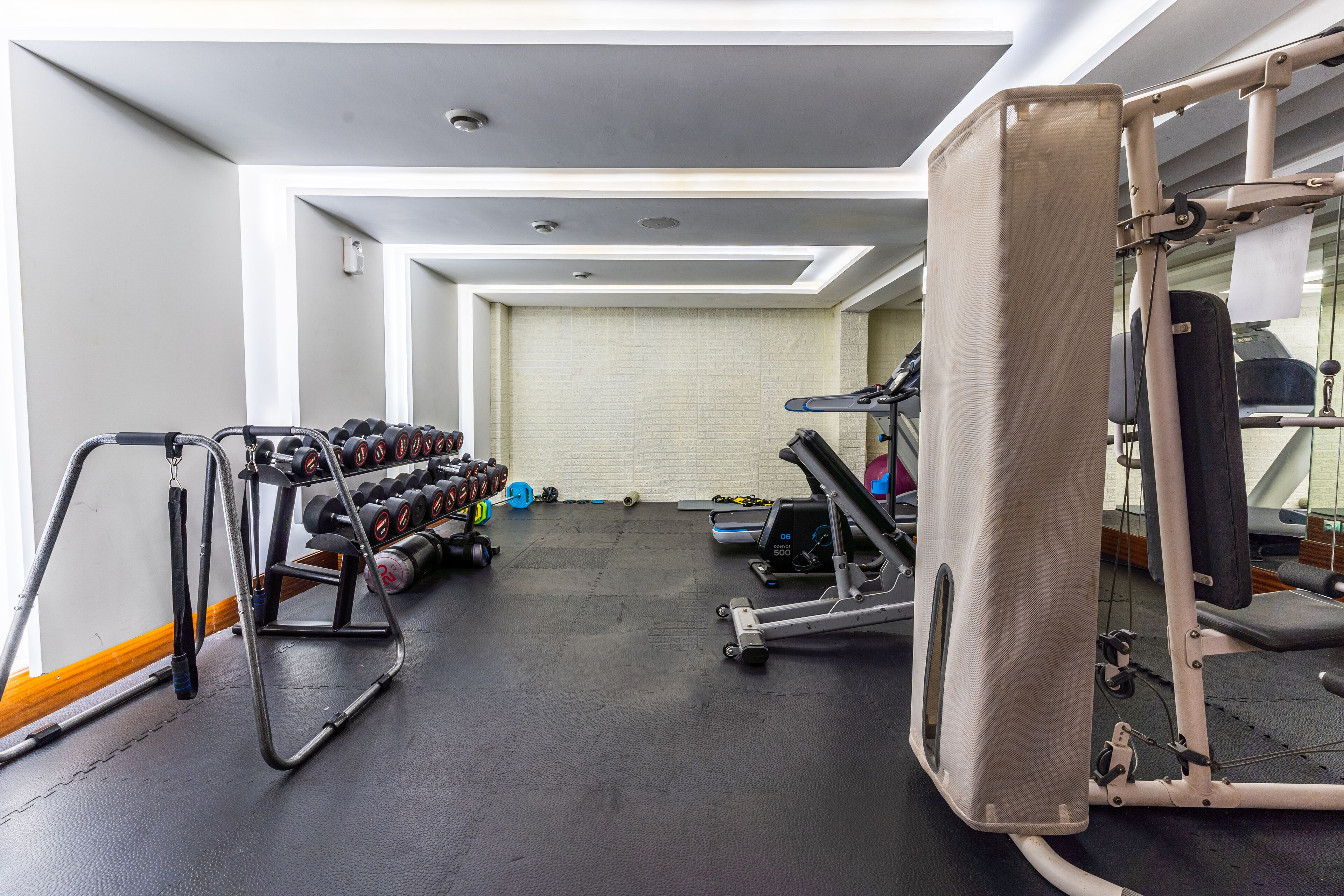 Ein Fitnessraum mit Trainingsgeräten, einem Spiegel und einem an der Wand befestigten Hantelständer.