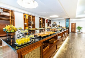 Un bufé con diversas opciones de comida y bebidas, detalles de madera y una planta en maceta.