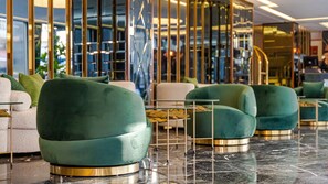 Een moderne lobby met groene bekleden fauteuils, een glazen bijzettafeltje en een marmeren vloer.