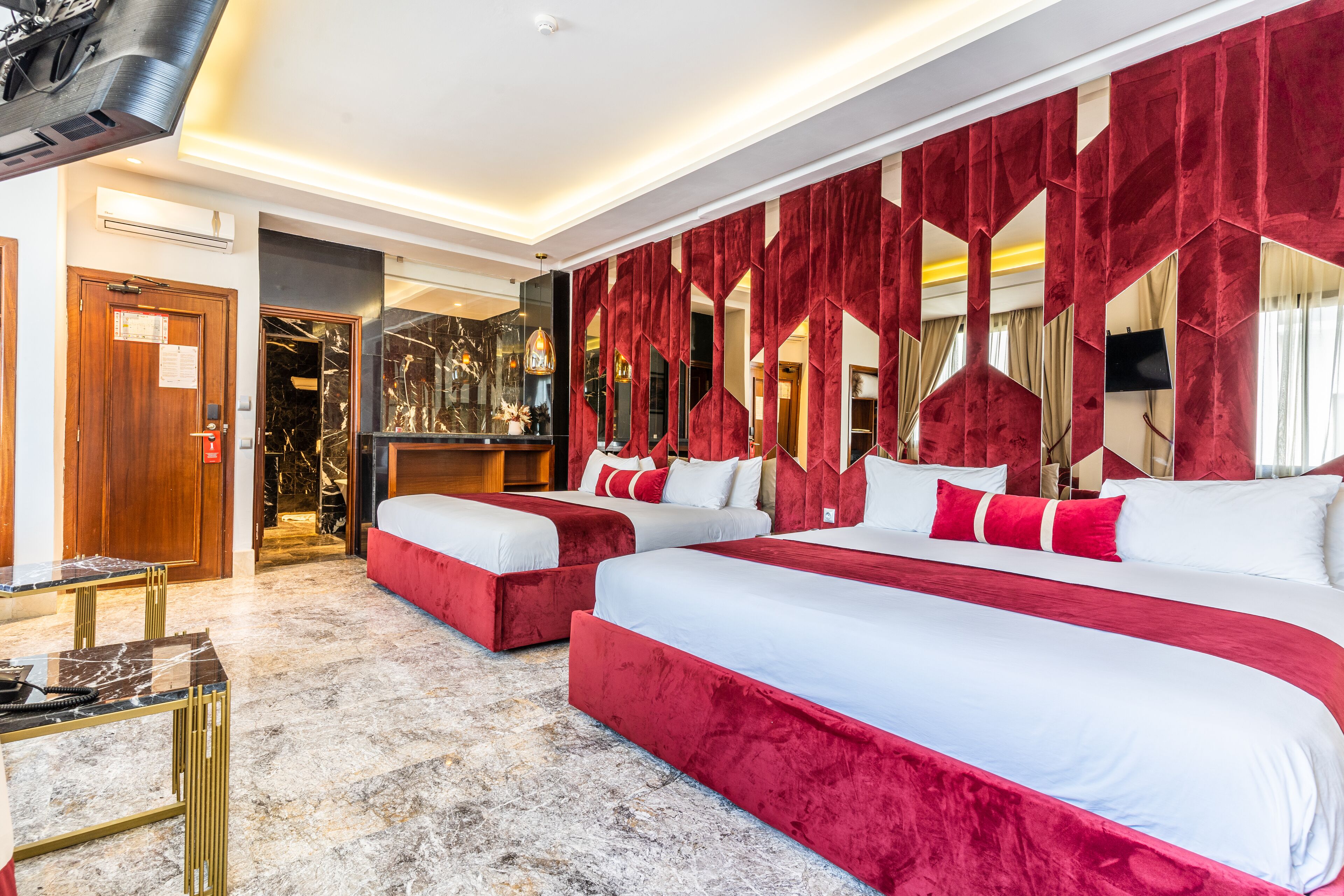 A hotel room with two beds, a marble floor, a wooden door, and a large mirror.